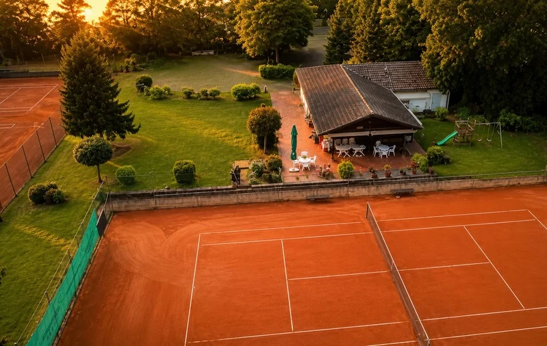 Aerial view of the tennis facility with clay courts, clubhouse, and green grounds at sunset