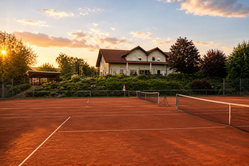 Tennis courts at KSV Steinklingen with clay surfaces during sunset with clubhouse in background