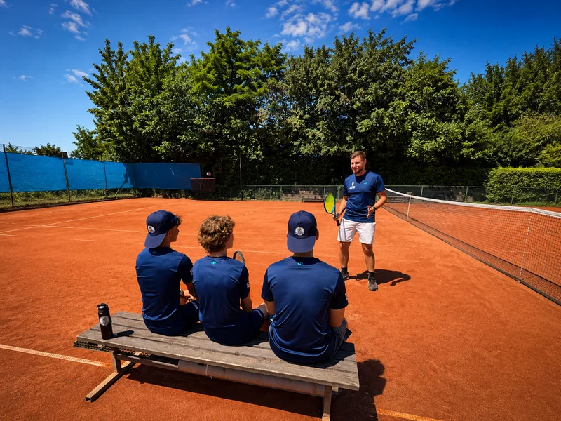 Trainer unterrichtet eine Gruppe von Schülern beim Gruppentraining auf der roten Sandplatzanlage