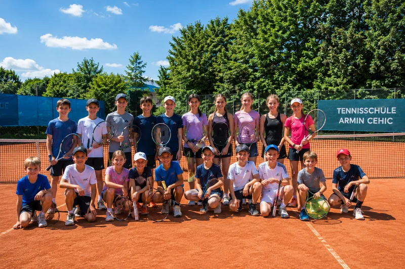 Gruppenfoto der Tennisschule Armin Cehic mit Trainern und Kindern auf dem roten Sandplatz mit blauem Vereinsschild im Hintergrund